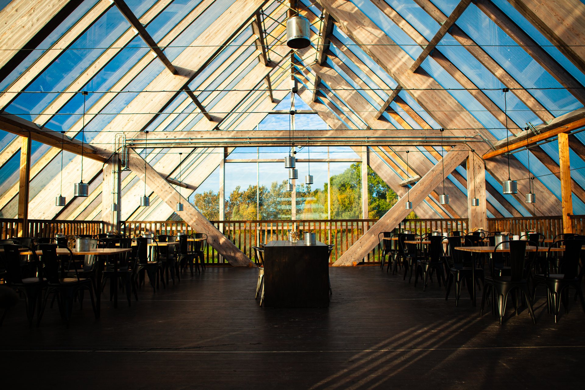 The tables and chairs under the high glass roof, with the trees outside the glass wall
